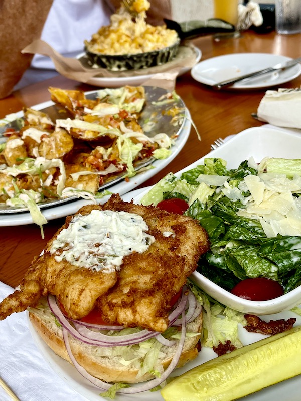 Several platters of food on a table including a breaded fish sandwich and a salad at Mudhen Brewing Wildwood NJ