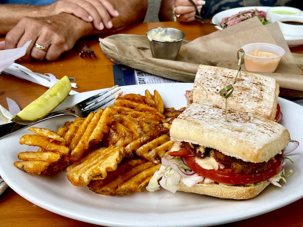 A white plate topped with waffle fries, pickle spear and a sandwich cut in half at Mudhen Brewing Wildwood NJ