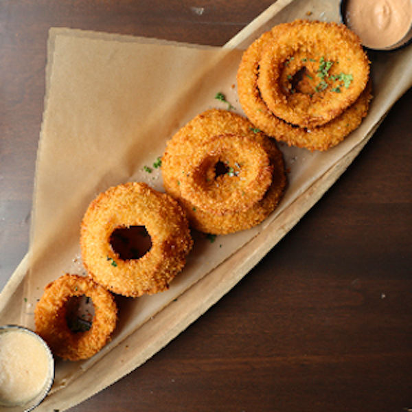 An oval platter topped with a triangle of brown paper and fried onion rings with two sauces at Mudhen Brewing Wildwood NJ