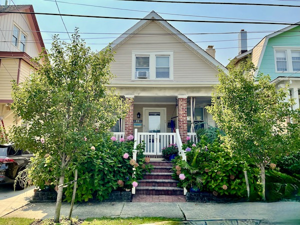 A house with brick stairs and front porch, pale yellow siding and lush bushes on Our Pilgrimage to the Jersey Shore