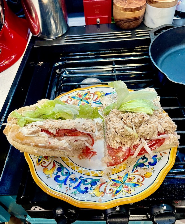 A yellow, white and blue plate topped with a tuna sub sandwich, sitting on the grate of a gas stove.