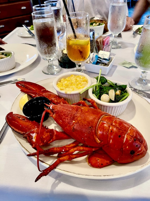 A large plate topped with a whole lobster, and two side dishes enjoyed while Revisiting Delaware Seashore State Park