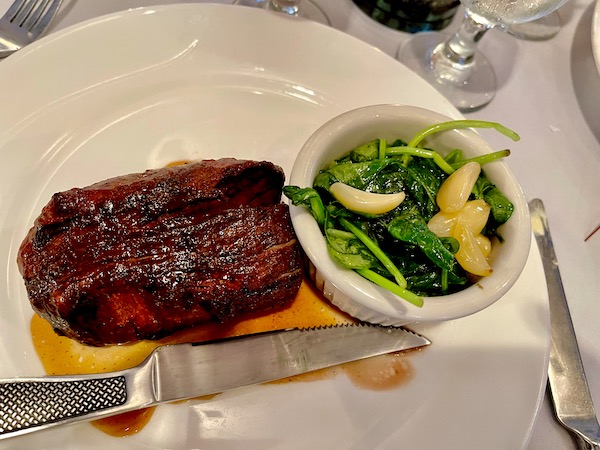 A large plate topped with a steak and a dish of spinach with garlic enjoyed while Revisiting Delaware Seashore State Park