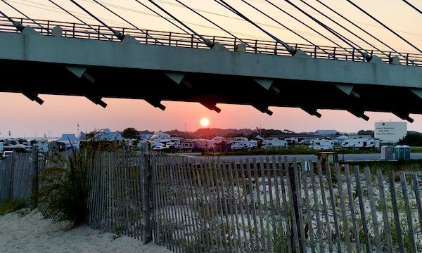 Beach, fence, bridge and sun setting over an RV park