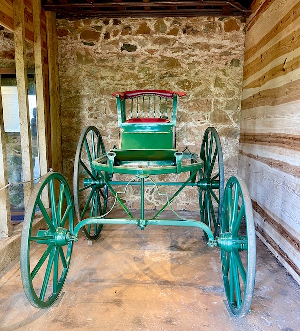 A stall with stone walls and a green horse drawn carriage.