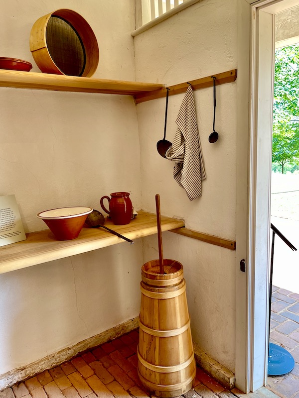 A room with kitchen artifacts on display including a wooden butter churn.