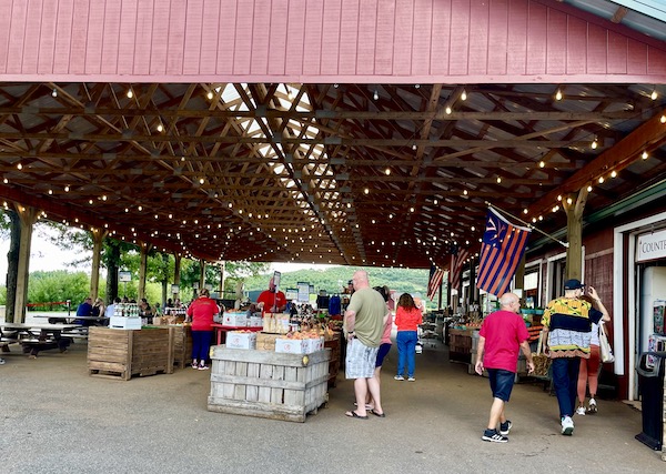 A farm market under roof busy with people shopping and lots of produce.