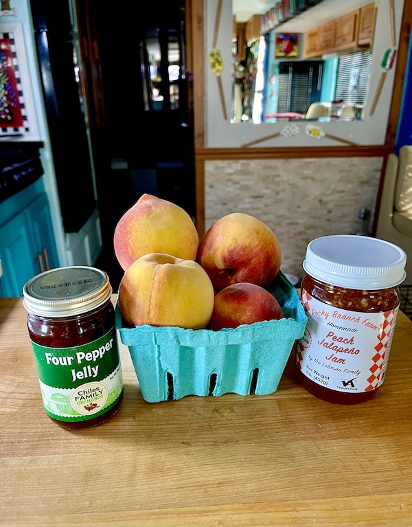 A wood board topped with two jars of preserves and a turquoise box filled with peaches.