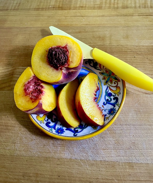 A blue and yellow plate topped with a partially sliced peach and a yellow knife.