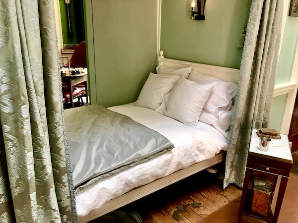 An alcove with light green walls and a feather bed with drapery pulled back
