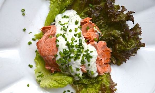 Poached salmon on a white plate with greens and white sauce is one of 7 Creative Ways to Serve Up Salmon