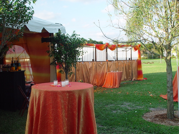 A lawn with a stable for two horses and a table draped with an orange cloth.