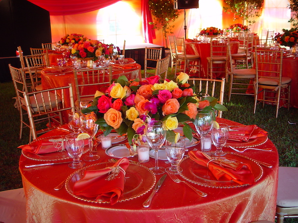 A table draped in shimmery orange cloth with a colorful floral centerpiece.