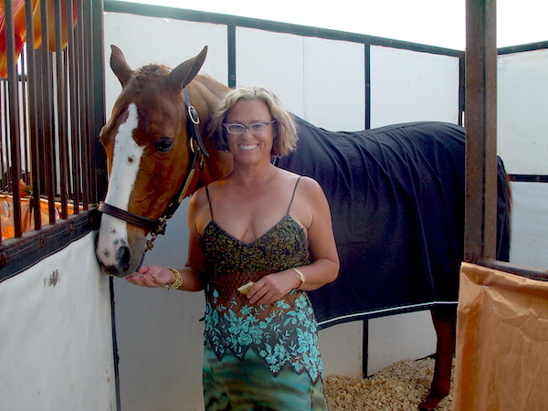 A woman in a teal and turquoise dress with her beautiful roan horse.