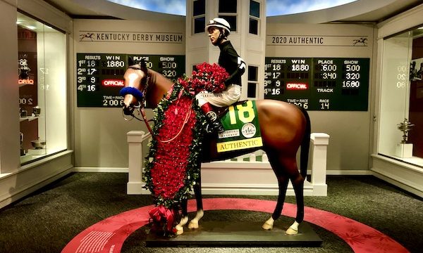 A red circle on the floor with a statue of a horse and jockey. The horse is wearing a blanket of red roses at Churchill Downs Louisville Kentucky
