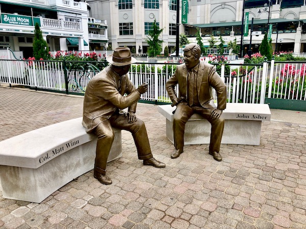 Bronze sculptures of two men who are deep in conversation. Each is sitting on a bench at Churchill Downs Louisville Kentucky