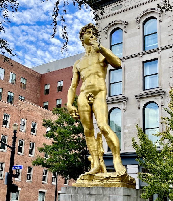 A gold statue of David standing tall in front of multistory buildings in Downtown Louisville Kentucky