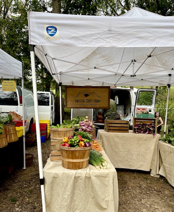 A farm stand set up with baskets of fresh produce under a white tent at the Farmers Market Nashville TN