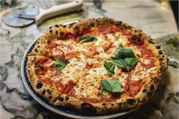 A whole pizza on a pizza pan topped with fresh basil leaves. Guess the most popular pizza toppings.