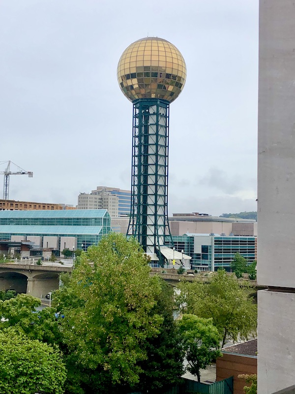 Trees and buildings with a tall cylinder topped with a gold sphere.