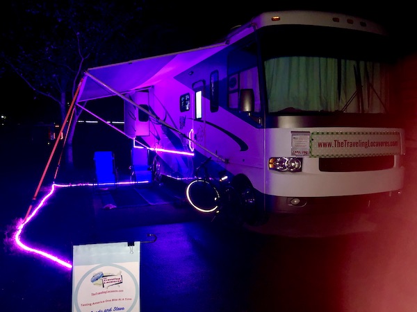 An RV lit in a purple glow at night.