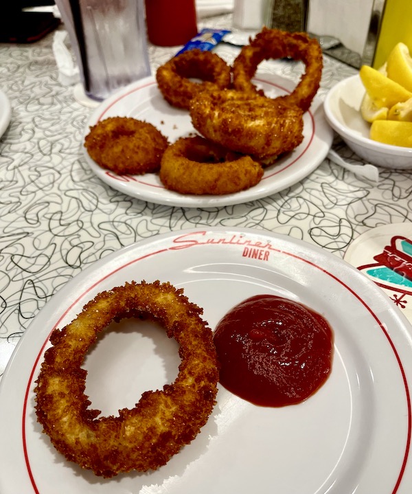 Two white plates with golden brown onion rings sitting on a formica tabletop at Sunliner Diner Pigeon Forge TN