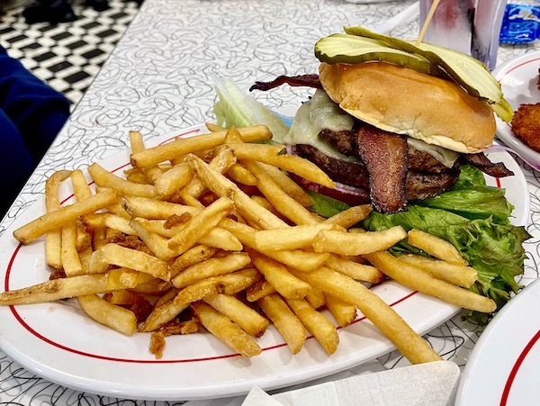 An oval white plate with a red line topped with lots of fries and a double bacon cheeseburger at Sunliner Diner Pigeon Forge TN