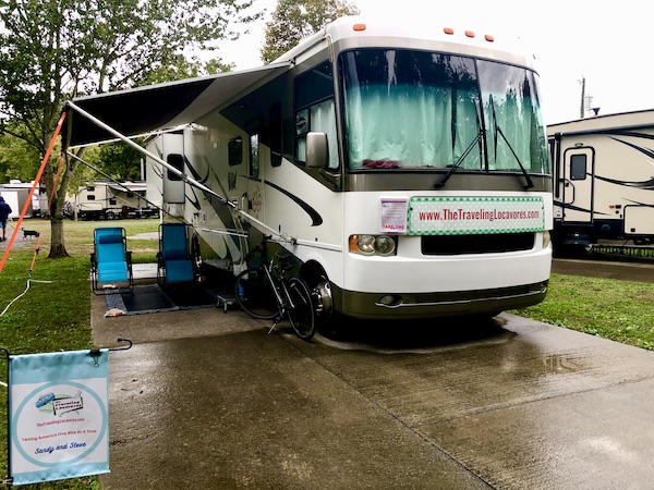 A white and tan RV with awning out and turquoise chairs on patio at an RV park in Pigeon Forge TN