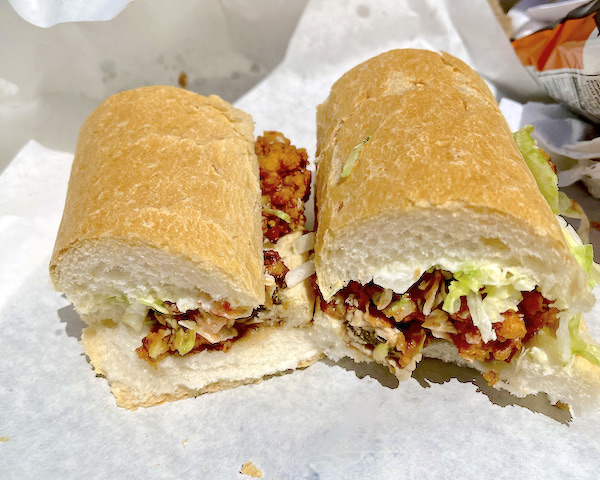 A Po' Boy sandwich cut in half, sitting on white deli paper from Best Po' Boys Domilise's vs Acme