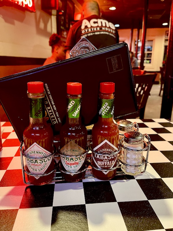 A trio of hot sauce bottles sitting on a black and white checkered tablecloth from Best Po' Boys Domilise's vs Acme