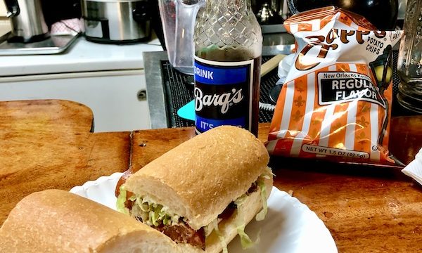 A white plate topped with a po' boy sandwich sitting on a wood bar from Best Po' Boys Domilise's vs Acme