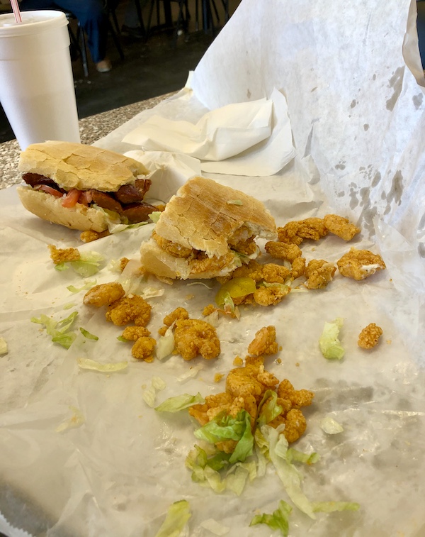 Two sandwiches on white paper with extra fried shrimp and lettuce spilling out.