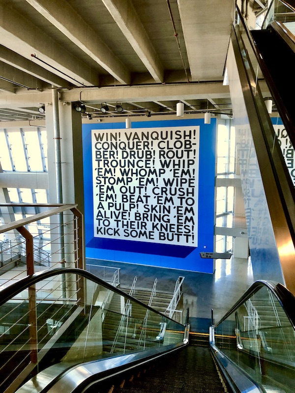 A white, blue and black sign with words of encouragement hanging by the escalators seen on our Dallas Cowboys Stadium Tour