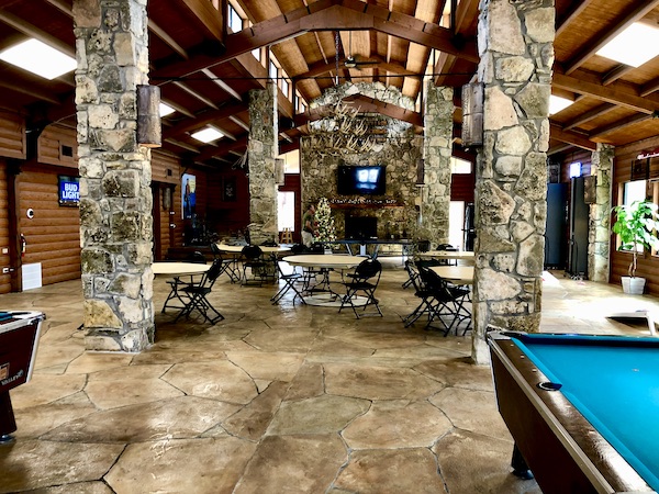 A huge room with stone pillars and walls, banquet tables, an 2 billiard tables.