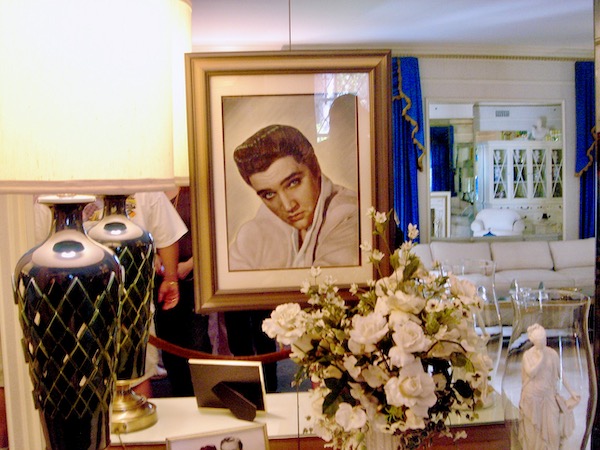 A portrait of Elvis Presley sitting on a table with white flowers and a black lamp at Graceland Home of the King.
