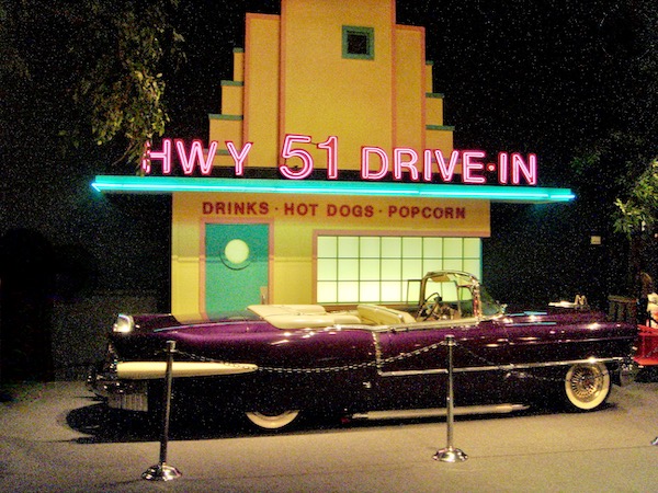 The front of a 50s diner with an aubergine colored Caddy convertible sitting in front.