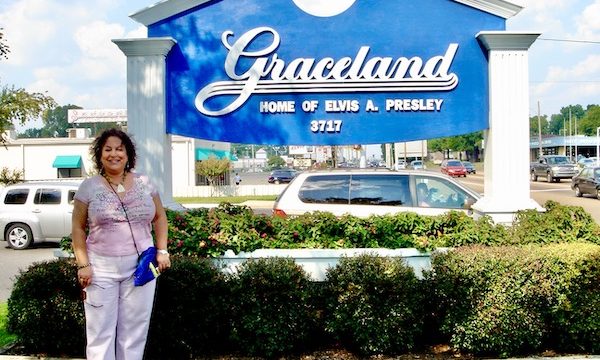 A woman in pink standing next to a blue and white sign for Graceland