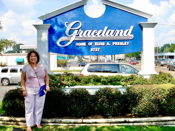 A woman in pink standing next to a blue and white sign for Graceland