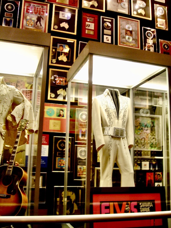 A display of white costumes that Elvis wore and awards on the wall.