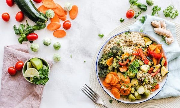 A white bowl and a fork on a white covered table. On the table and in the bowl are a rainbow of vegetables. From Keeping An Open Mind Will Improve Your Relationship With Food