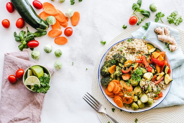 A white bowl and a fork on a white covered table. On the table and in the bowl are a rainbow of vegetables. From Keeping An Open Mind Will Improve Your Relationship With Food