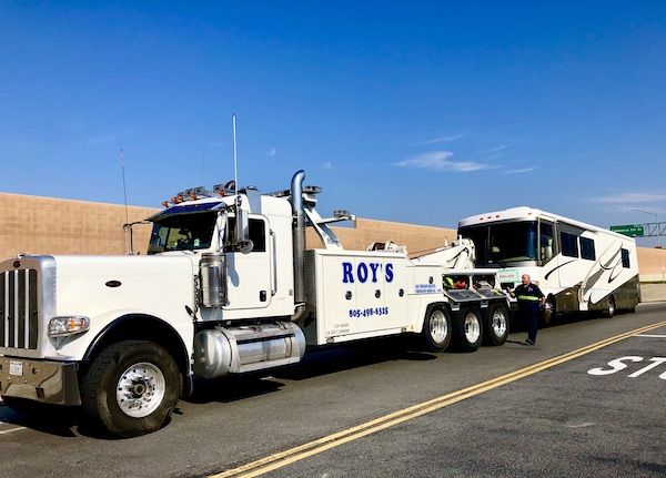 A man walking beside a giant tow truck to hook up an RV