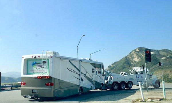 A white and beige RV being towed by a white tow truck in order to get new brakes for Ladybug.
