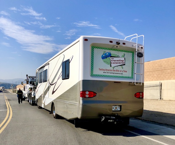 A beige and white RV lined up behind a tow truck.
