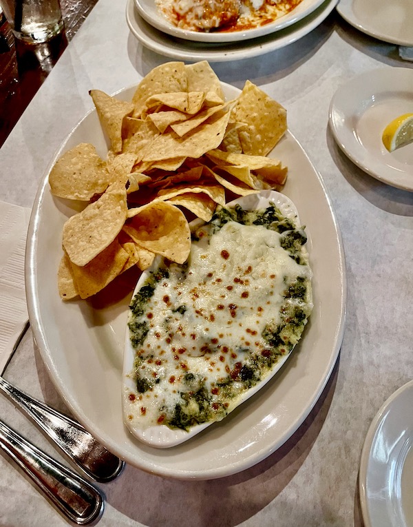 A large oval platter topped with a cheesy green dip and fresh tortilla chips at Nik's Italian Kitchen Austin TX