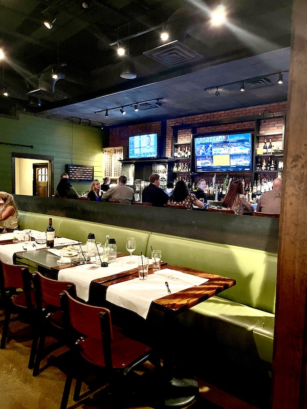 The interior of a restaurant with TVs at the bar and yellow/green banquettes in Austin TX.