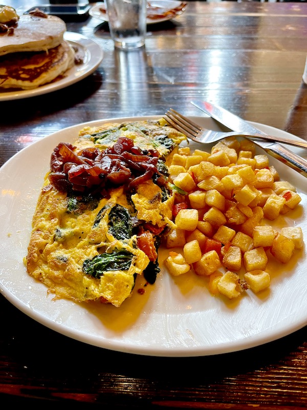 A white plate topped with a vegetable studded cheese omelet and home fried potatoes.