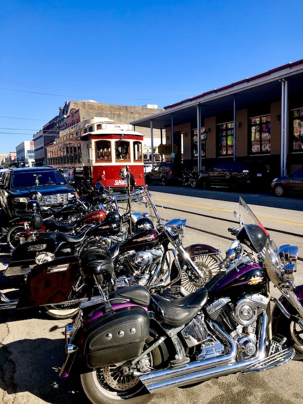 A red and white street car in the center of the street and a long row of motorcycles park by the curb.