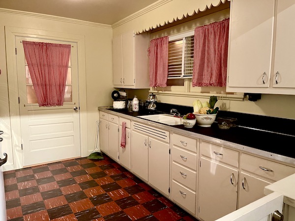 An all white vintage kitchen with black countertops.