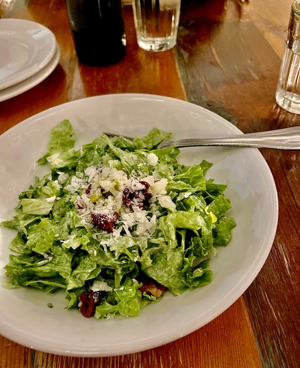 A white plate topped with lettuce, tomatoes and cheese as a fork rests on the side of the plate.